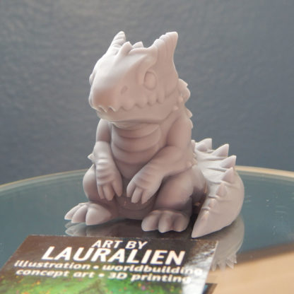A small, unpainted figurine of a cute lizard monster.