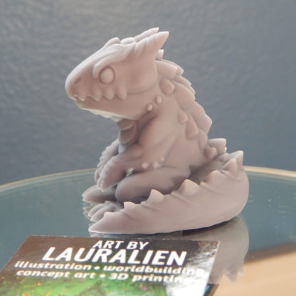 A small, unpainted figurine of a cute lizard monster.